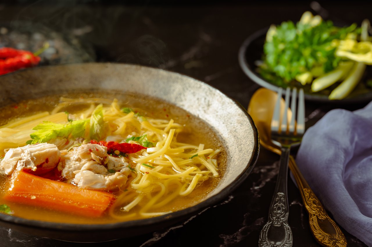 about-us Capture of a flavorful chicken noodle soup with garnishes in a rustic setting.