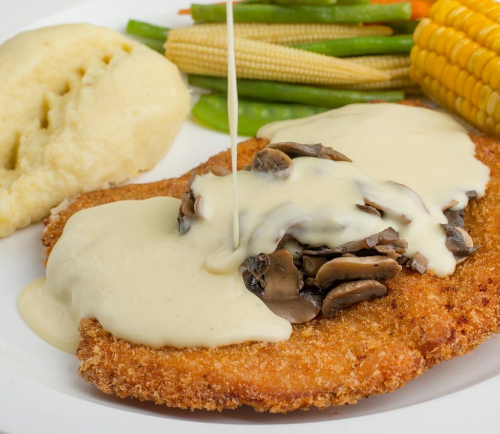 Savory breaded cutlet topped with creamy mushroom sauce, served with fresh vegetables.
